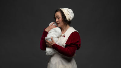 Barnmorskan håller en nyfödd baby mot sin axel. Skådespelare Nina Hukkinen.