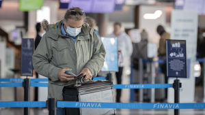Passagerare med munskydd och liten kappsäck på Helsingfors-Vanda flygplats.