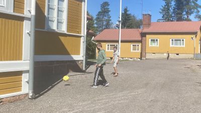 Två skolelever med munskydd spelar fotboll på gårdsplan.