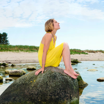 Kvinna sitter på sten i strandbrynet.