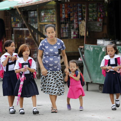 En filippinsk mamma tar sina barn till skolan i huvudstaden Manila.