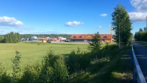 Andelslaget Varuboden-Osla vill bygga en Prisma i Läpp i Karis. En grön äng och till höger skymtar en asfalterad väg. Längre bort synd en ABC-bränslestation samt parkerade långtradare. Blå himmel, solsken.