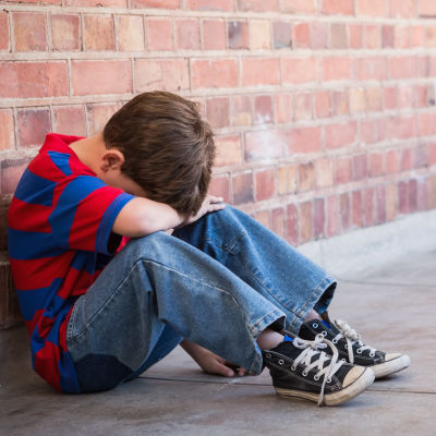 Ett barn ser ut att vara ledsen och sitter i en korridor och täcker sitt ansikte med armarna.