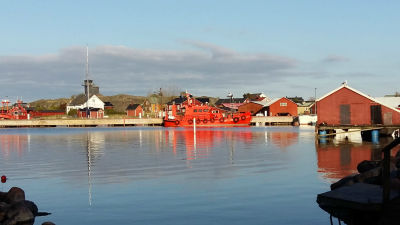 Hamnen i Utö med båthus och en lotskutter som speglas i vattnet.
