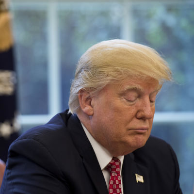 Donald Trump stirrar ner i bordet iklädd kostym i ett arbetsrum som syns suddigt i bakgrunden.