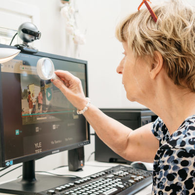 Nainen katsoo suurennuslasilla tietokoneen näyttöä.