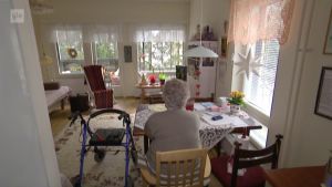 För Alzheimersjuka Hilkka Jämsä känns hemmet inte längre tryggt. Äldre ensam kvinna tittar ut i vardagsrummet.