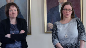 Piia Nordström och Jaana Pönni berättade om fiskvägsplanerna på gamla stadshuset i Ekenäs. Två kvinnor som står framför två porträtt som föreställer män.