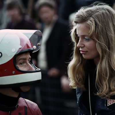 Jarno Saarinen med motorcykelhjälm på huvudet pratar med sin hustru Soili Saarinen med långt blont hår.