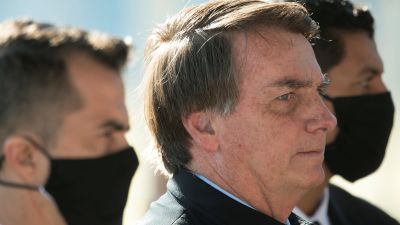 Brasiliens president Jair Bolsonaro utanansiktsmask. Bredvid honom står två män med ansiktsmask
