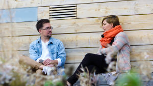 Adam Guarnieri kände sig aldrig hemma i rollen som flicka. Idag är han ofta en anlitad föreläsare om transfrågor. Adam Guarnieri och Maria Sundblom Lindberg i samspråk utomhus framför ljus trävägg på ön Lonnan i Helsingfors.