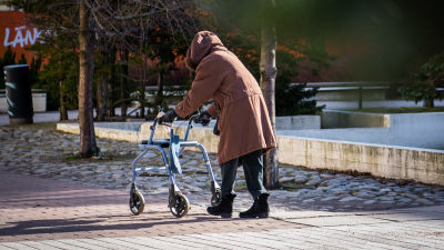 Vanhus rollaattorin kanssa kävelemässä kohti kauppaa.
