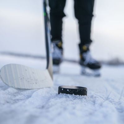 En puck och en ishockeyklubba på snöig isbana.