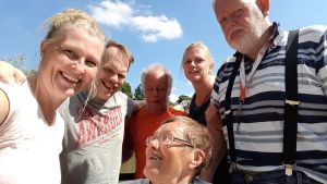 Kårkulla erbjuder svenskspråkig specialomsorg och handikappservice för personer med utvecklingsstörning eller annan funktionsnedsättning. Bilden är en av Kårkullas pressbilder. Kommunernas kritik är allmän och berör inte de personer som syns på bilden. Medelålders och lite äldre personer med funktionsnedsättning samt två yngre vårdare ser glada ut i en gruppbild. Sol och sommar.