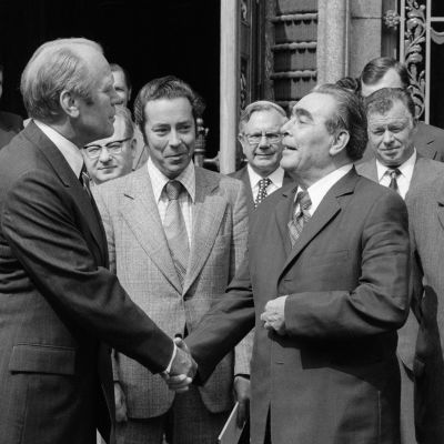 Svartvitt foto där USA:s president Gerald Ford och Sovjetunionens president Leonid Brezjnev skakar hand under Helsingforskonferensen 1975 omgivna av 