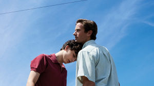 Call Me by Your Name Elio (Timothée Chalamet) nojaa päätään Oliverin (Armie Hammer) rintaa vasten. Sininen taivas taustalla.