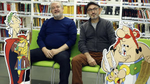 Vuodesta 2012 lähtien Asterix -sarjakuvia on käsikirjoittanut Jean-Yves Ferri ja kuvittanut Didier Conrad Asterix-sarjakuvien käsikirjoittaja Jean-Yves Ferri ja kuvittaja Didier Conrad istuvat pahvisten sarjakuvahahmojen välissä