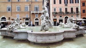 Monin veistoksin koristeltu suihkulähde Piazza Navonalla Roomassa, taustalla punertavia rakennuksia.