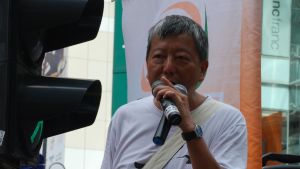 Lee Cheuk-yan har ordnat oräkneliga demonstrationer sedan han blev politiskt aktiv som studerande. Han säger att han inte accepterar att det är förbjudet att delta i en fredlig protest. Lee Cheuk-yan står med mikrofon i hand framför en skara människor. trationer sedan han blev politiskt aktiv som studerande.