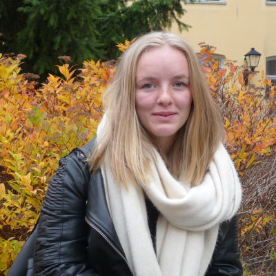 Julia Degerth profilbild, fotat utomhus en lövklädd buske i gula, röda och bruna färger bakom Julia.