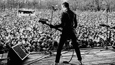 Paul Simonon The Clash -yhtyeestä lavallav selin, edessä yleisömeri. Kuva vuodelta 1978, dokumenttielokuvasta White Riot.