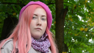 Estradpoeten Rosanna Fellman rimmar ganska mycket då hon uppträder, men i bokform kan det kännas styltigt. – På sitt sätt kommer väl rim och meter tillbaka. Men nu får det existera olika typers poesi samtidigt så de kommer inte att ta över, säger hon. en kvinna i rosa hår och grå jacka står bland grönskande träd