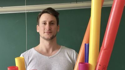 Man står framför svarta tavlan i klassrum, framför sig har han färgglada plaströr.