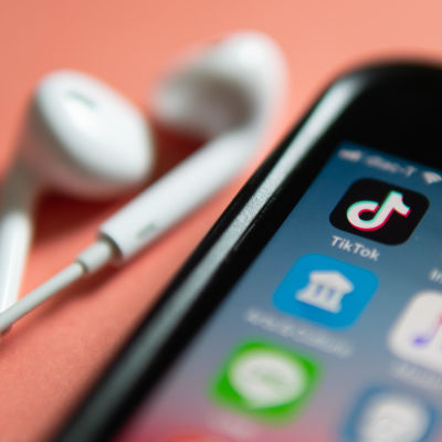 En telefon och ett par hörlurar ligger på ett persikofärgat bord. På telefonen syns olika appar, bland annat Tiktok och Instagram.
