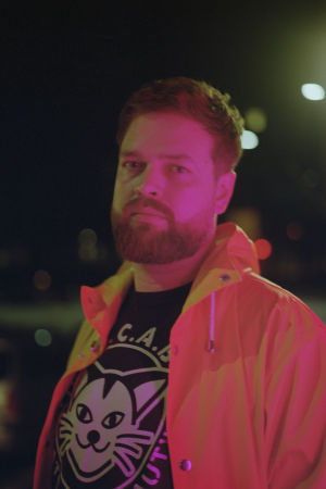 Johannes Ekholm. På bilden syns författaren Johannes Ekholm klädd i en gul jacka och svart tröja med ett vitt kattmönster på.