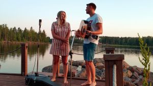 Josefin tillsammans med sin bror Jonas som producerat Klöveråtton. Bilden är tagen på bryggan vid sommarstugan i Oxkangar där syskonen ofta brukar sitta och spela. Josefin och Jonas Sirén står på bryggan med en gitarr och mikrofoner.