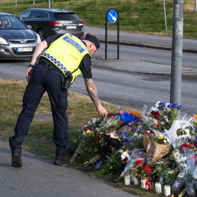 En polis lägger ner blommor vid en lyktstolpe där det samlats blombuketter.