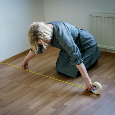 Nainen mittailemassa kontallaan lattialla tyhjässä asunnossa.