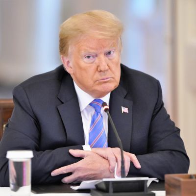 USA:s president Donald Trump ser allvarlig ut och sitter vid ett bord med sina armbågar på bordet. Framför honom finns en mikrofon.