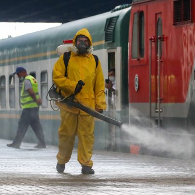En man i gul skyddsutrustning desinfierar framför ett tåg. 