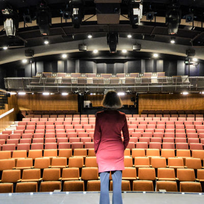 Kvinna i brun page ser ut över en tom teatersalong.