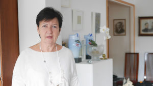 Eva Auranen tar emot hemma hos sig, och berättar att sonen trivs bra i sitt nya hem i Esbo. Service på svenska upplever både mor och son som viktigt. Eva Auranen i sin lägenhet med vaser och tavlor i bakgrunden
