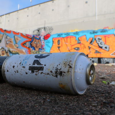 Två tomma sprayfärgsburkar ligger framför en vägg prydd av graffiti. 
