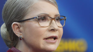 Julija Tymosjenko eller Juri Tymosjenko? Bland annat den utmaningen ställdes de ukrainska väljarna inför i Ukrainas presidentval 2019. Porträttbild på Julia Tymosjenko. Hon bär glasögon och en klassisk låg hårknut i nacken. I bakgrunden syns landets blågula färger.