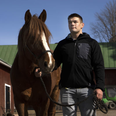 Arvi Savolainen är iklädd jacka och leder en häst.
