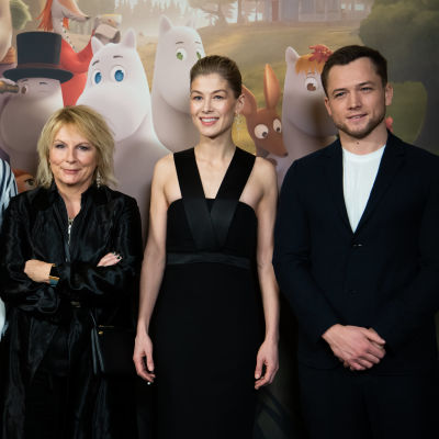 Edvin Endre, Jennifer Saunders, Rosamund Pike ja Taron Egerton seisovat muumien kuvausseinän edessä vierekkäin hymyillen.