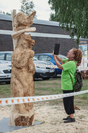 Minna Haveri fotograferar Leevi Halonens verk. Rastapäinen nainen ottaa valokuvaa karhun mallisesta puuveistoksesta