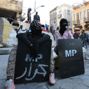 I Bagdad har helgens våldsammaste sammandraningar pågått kring centralbanken Demonstranter med sköldar sitter på gatan framför en barrikad i Bagdad