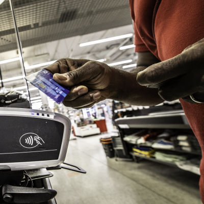 En hand håller i ett blått visakort och för det mot en betalningsautomat vid en kassa.