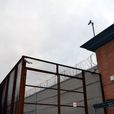 Staket, taggtråd och övervakningskameror vid fängelsemur.