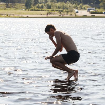 En pojke hoppar i vattnet vid en badstrand.