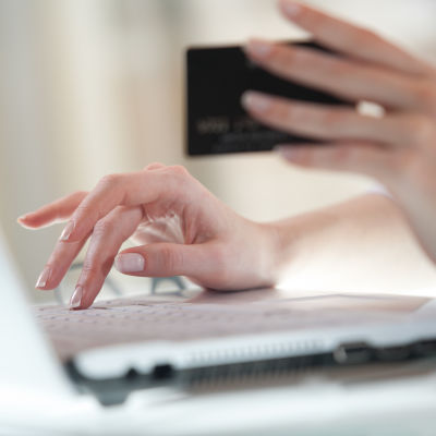 En person håller upp ett bankkort och knappar samtidigt på ett tangentbord.