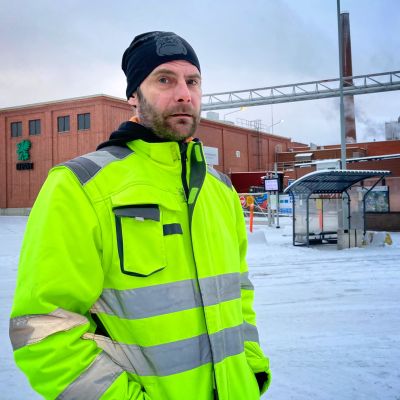 UPM:n  Tervasaaren tehtaan pääluottamusmies Tomi Eerola seisoo tehtaan edustalla keltaisessa työtakissa. 