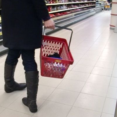 Nainen kantaa ostoskoria kaupan käytävällä.