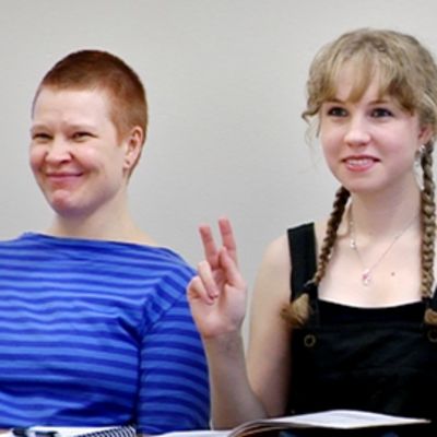 Kaksi viittomakielen opiskelijaa harjoittelevat k-kirjaimen viittomista.