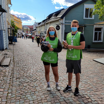 En kille och en tjej iklädda gröna västar står på en mellangatan i en stad.